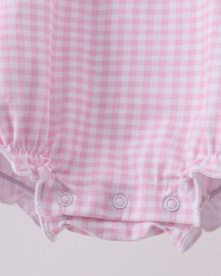 Close-up of a pink and white gingham baby romper with ruffled trim and three white snap closures at the bottom.