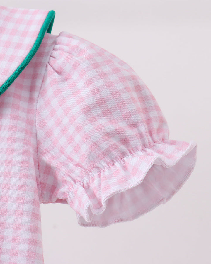 Close-up of a pink and white gingham baby dress with a ruffled puff sleeve and a green collar trim, shown against a plain light background.