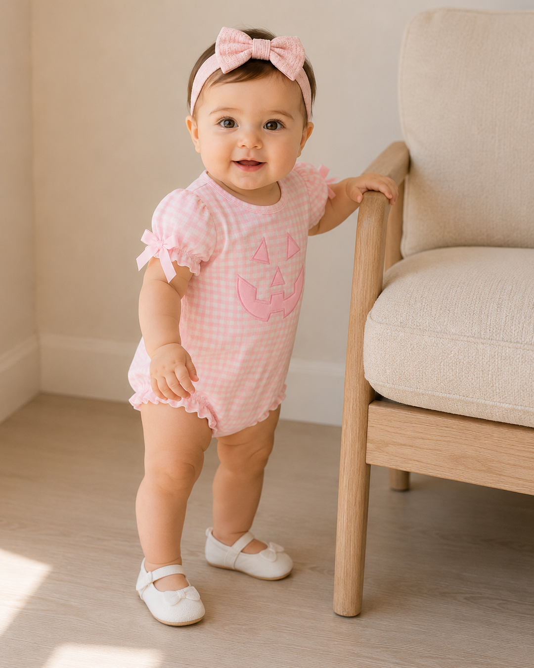 Pink gingham baby bubble romper with jack-o-lantern applique, ruffle sleeves, worn with bow headband