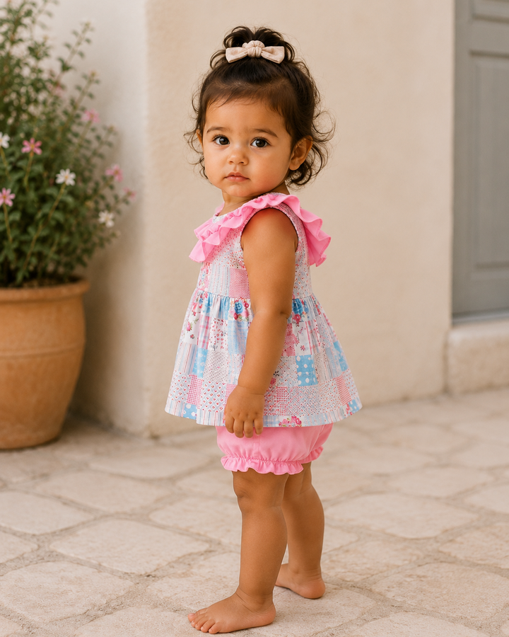 Young child wearing a colorful dress with ruffles standing on a stone patio.
