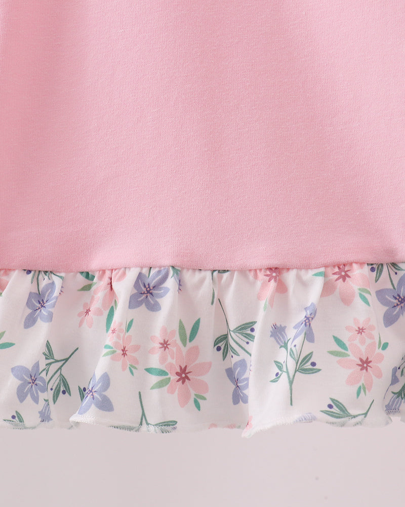 Close-up of a pink garment with a ruffled hem featuring a white background and a pastel floral print in pink, purple, and green.
