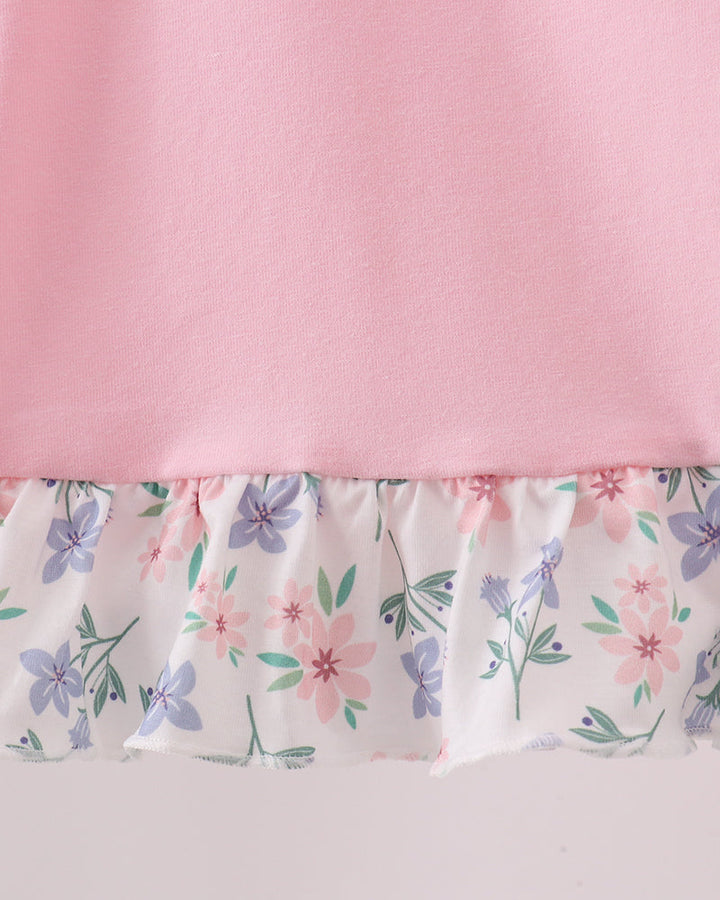 Close-up of a pink garment with a ruffled hem featuring a white background and a pastel floral print in pink, purple, and green.