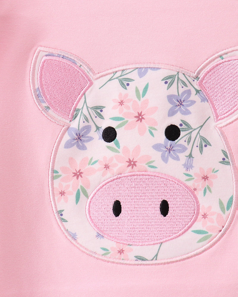Close-up of a pink garment featuring an applique pig face patch with a floral print, pink ears, and embroidered black eyes and snout details.