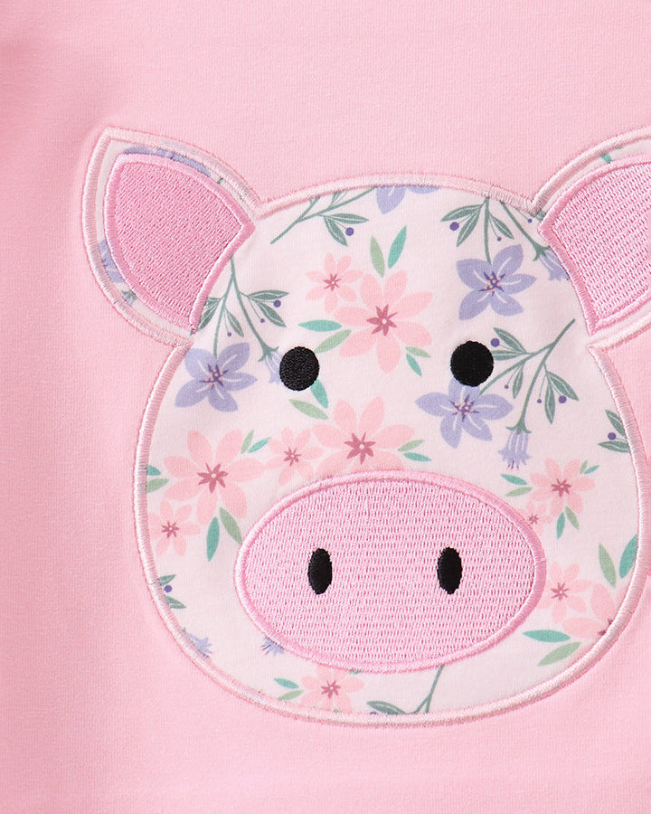 Close-up of a pink garment featuring an applique pig face patch with a floral print, pink ears, and embroidered black eyes and snout details.