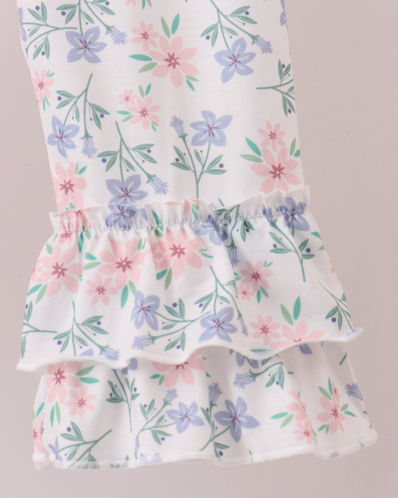 A close-up of a white tiered ruffle garment featuring a delicate floral print with pink, purple, and green flowers and leaves.