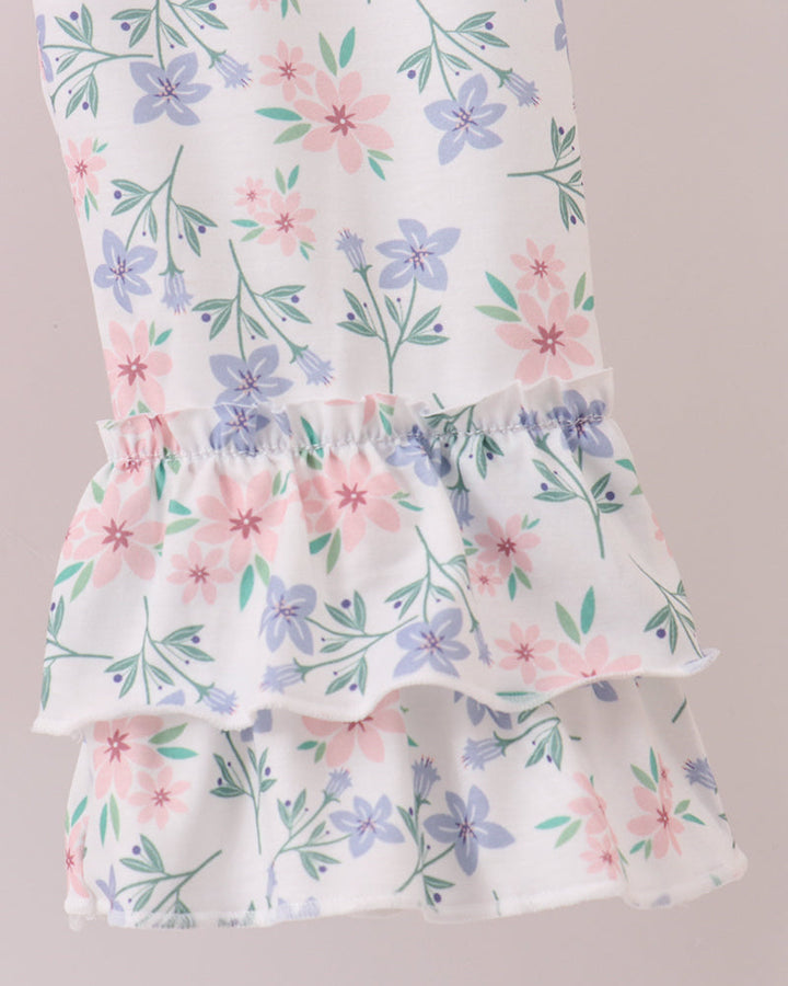 A close-up of a white tiered ruffle garment featuring a delicate floral print with pink, purple, and green flowers and leaves.