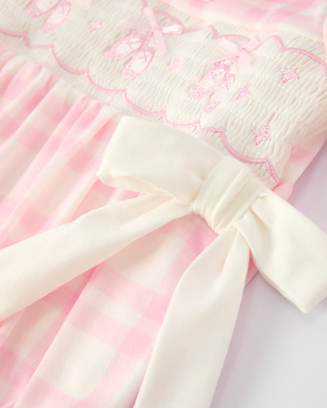 Pink plaid romper with white bow detail at waist and puffed skirt panels