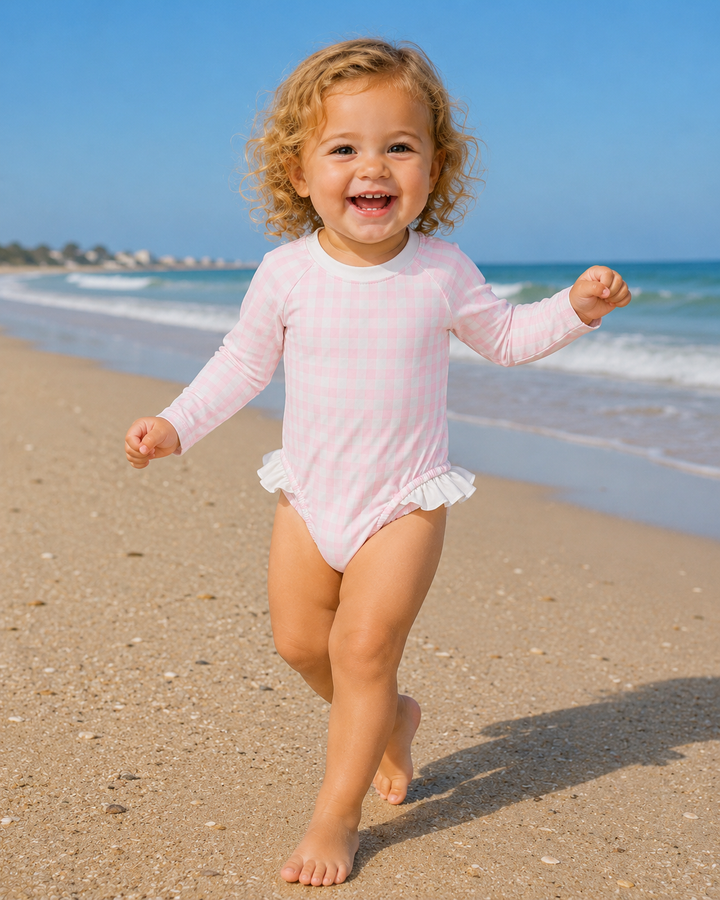 Child in a pink swimsuit running on a sandy beach with ocean and clear sky in the background