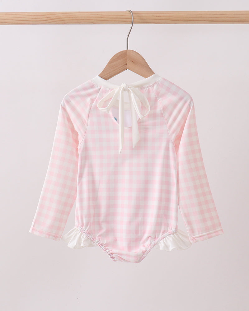 Pink checkered rashguard with long sleeves on a wooden hanger against a white background
