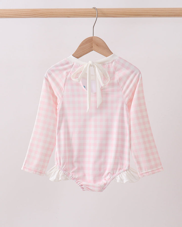 Pink checkered rashguard with long sleeves on a wooden hanger against a white background
