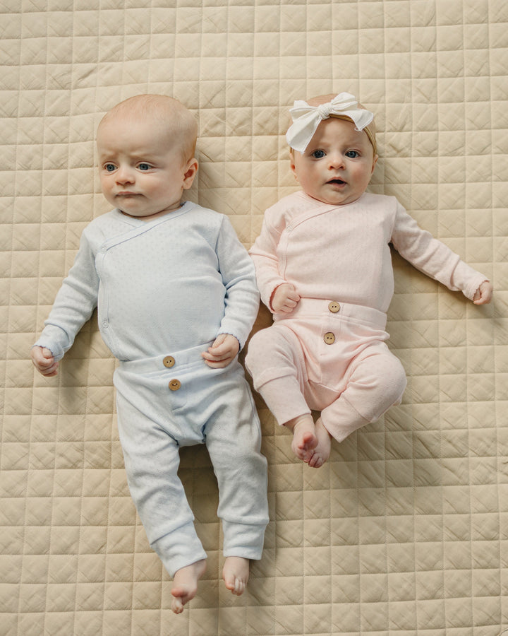 Two babies lying on a round, quilted mat wearing matching outfits.