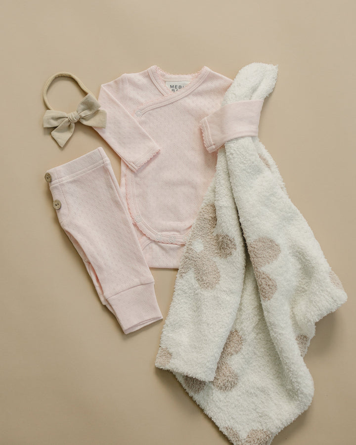 Baby clothing set with pink outfit, pants, blanket, and headband on a beige background