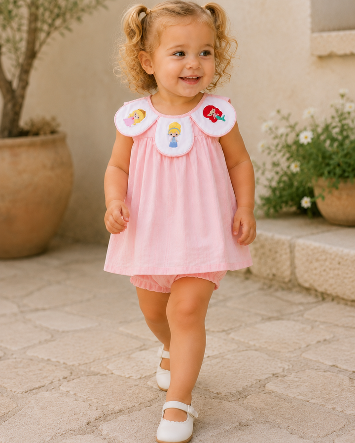Young girl in a pink dress with character patches walking outdoors.