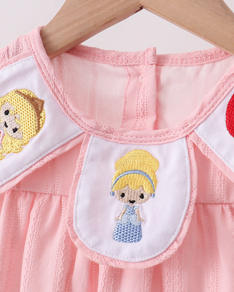 Close-up of a pink dress with embroidered character patches on a white background
