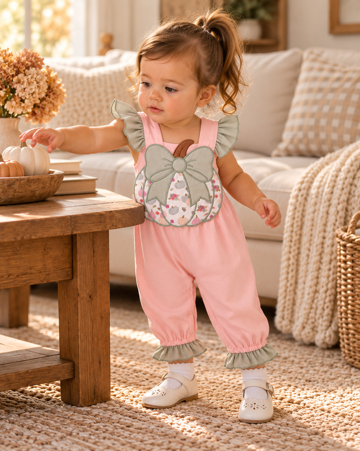 Pink toddler romper with pumpkin bow appliqué, ruffle sleeves, and ruffle cuffs.