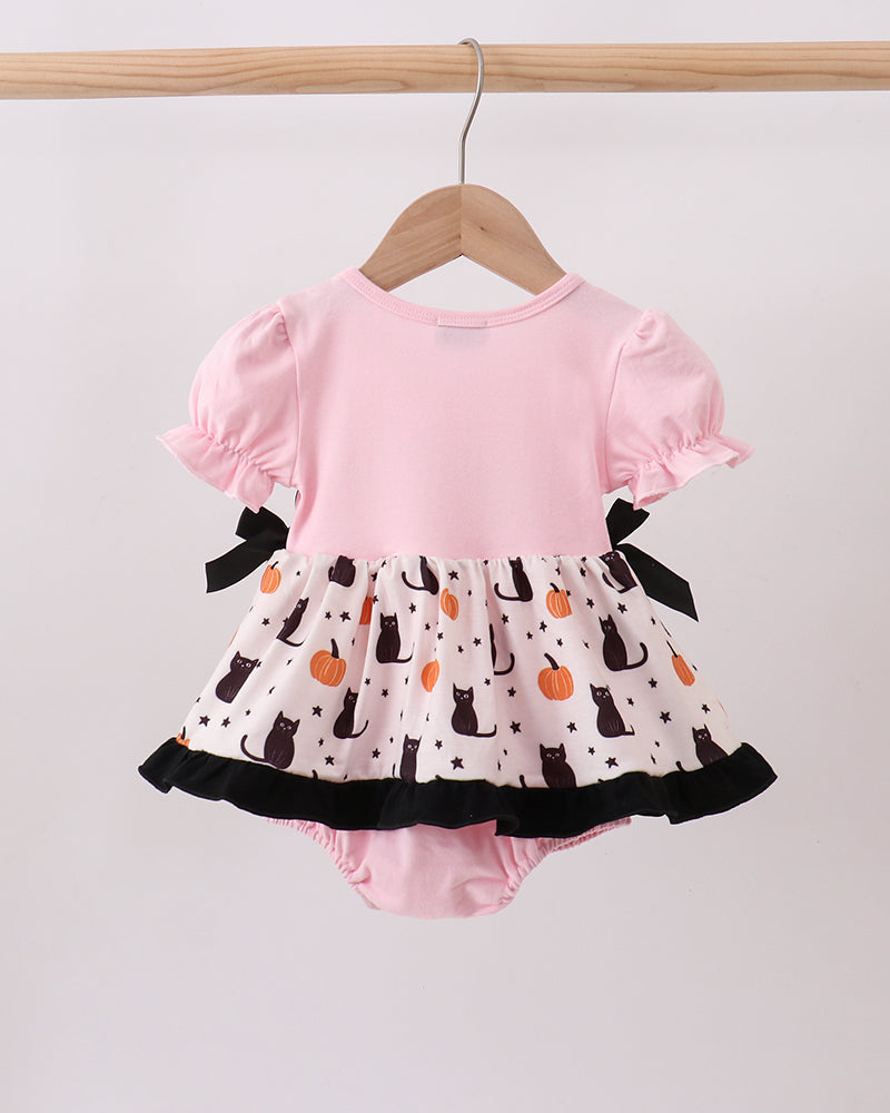 A baby romper with a light pink top and a white ruffled skirt featuring a black cat and orange pumpkin pattern, hanging on a wooden hanger.