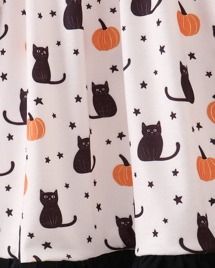 A close-up of a curtain featuring a Halloween pattern with black cats, orange pumpkins, and small black stars on an off-white background, finished with a black ruffled hem.