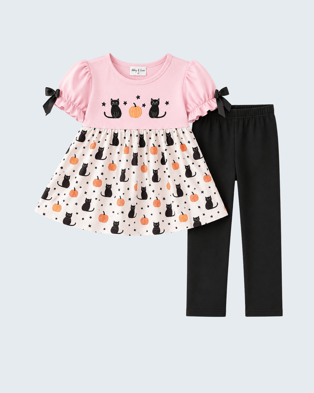 A toddler girl's two-piece Halloween outfit set featuring a pink short-sleeve top with black cat and pumpkin graphics, a white polka-dot skirt with black cat and pumpkin prints, and solid black leggings.