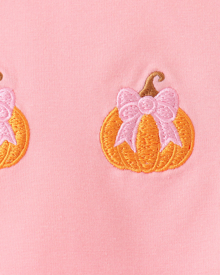 Close-up of pink top with orange pumpkin embroidery and pink bow accents