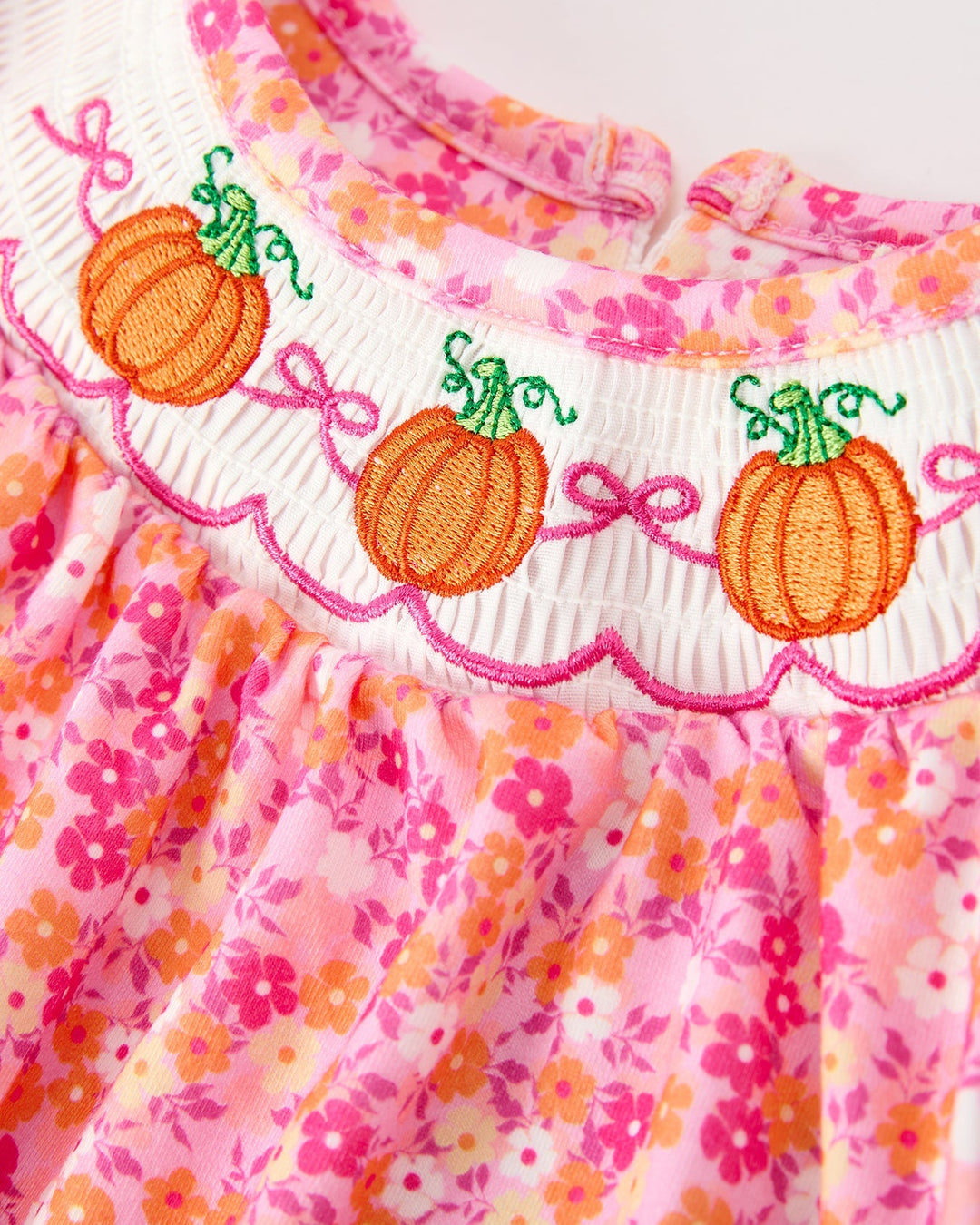 Pink floral bubble romper with embroidered orange pumpkins and rickrack trim.