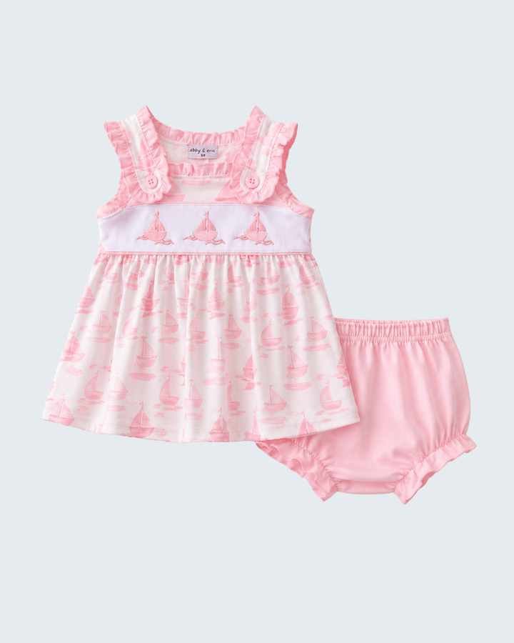 Pink baby dress with ruffled top and matching bloomers on a light gray background