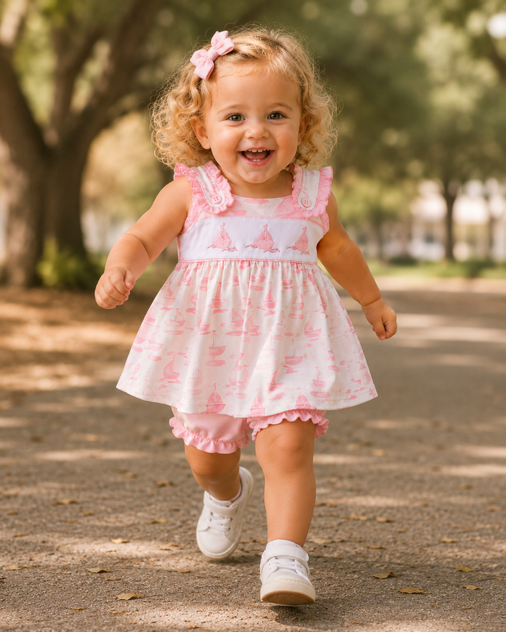 Child in a pink and white dress running outdoors on a path with trees in the background