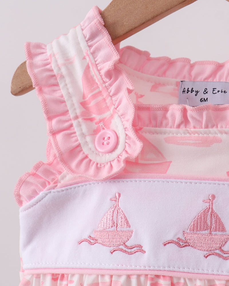 Pink and white dress with ruffles and sailboat embroidery on a hanger.