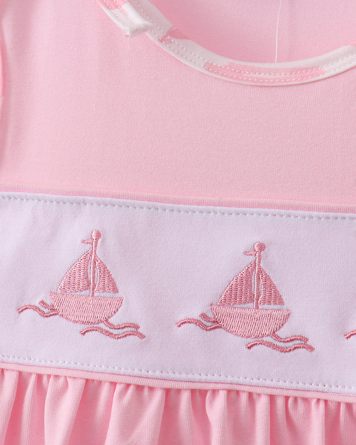 Close-up of a pink dress with embroidered sailboats on a white background