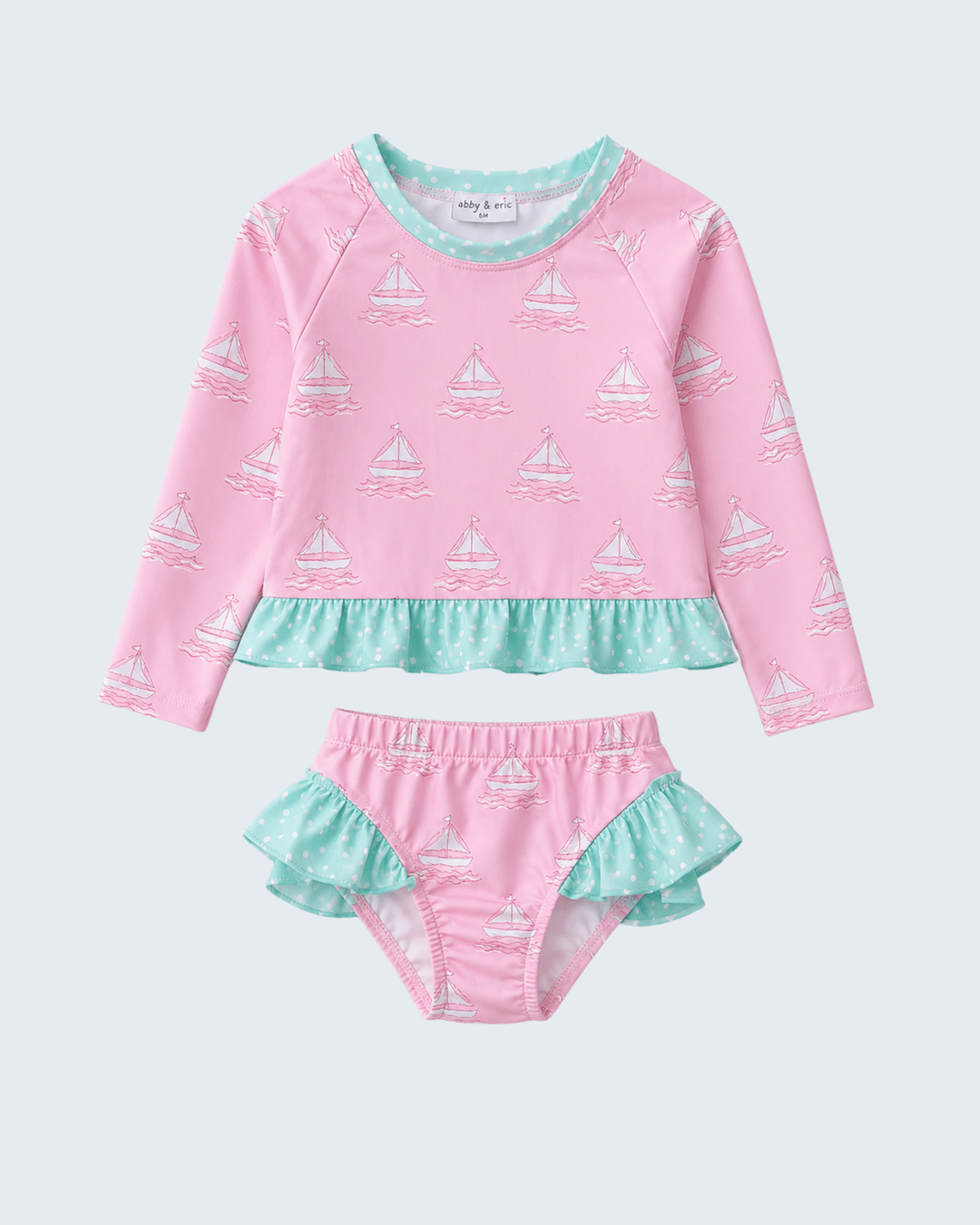 Pink and green children's swimsuit set with sailboat pattern on a light gray background
