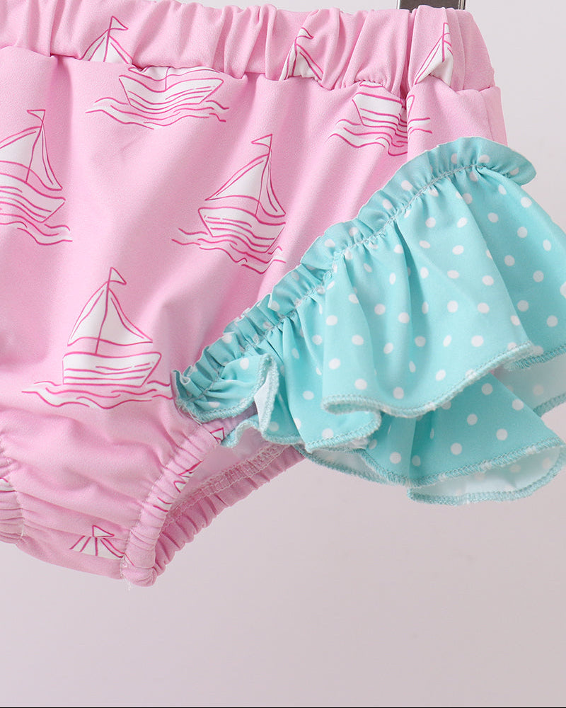 Pink and teal swim bottoms with sailboat and polka dot patterns on a white background.