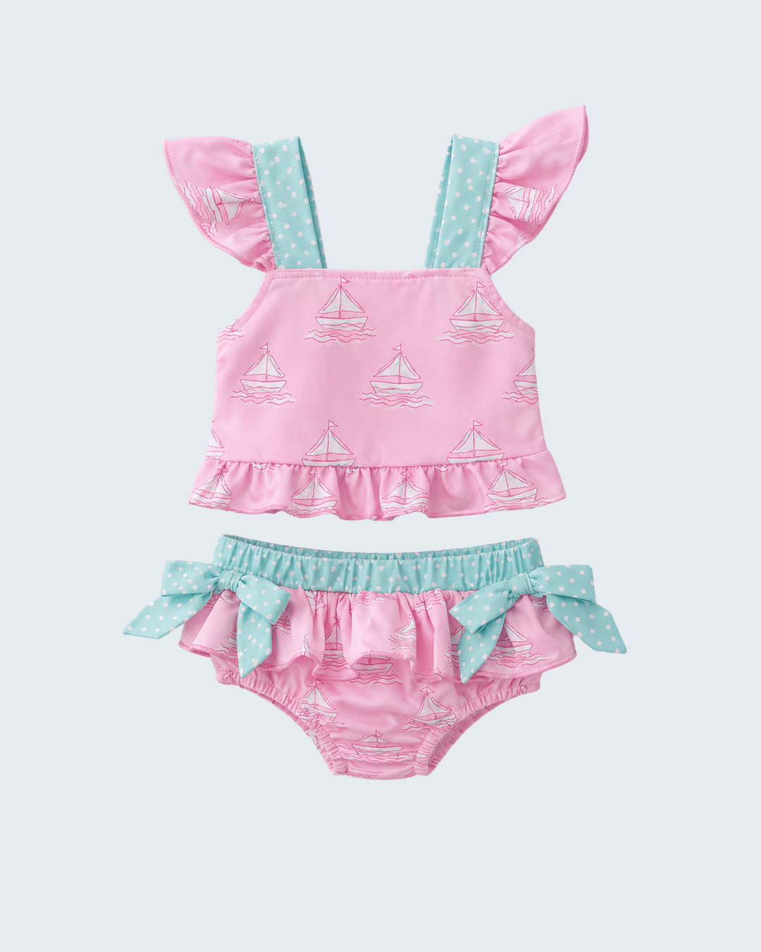Pink and blue baby swimsuit set with sailboat pattern on a light gray background