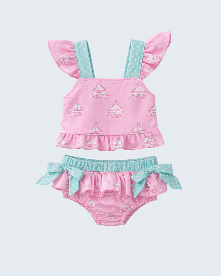 Pink and blue baby swimsuit set with sailboat pattern on a light gray background