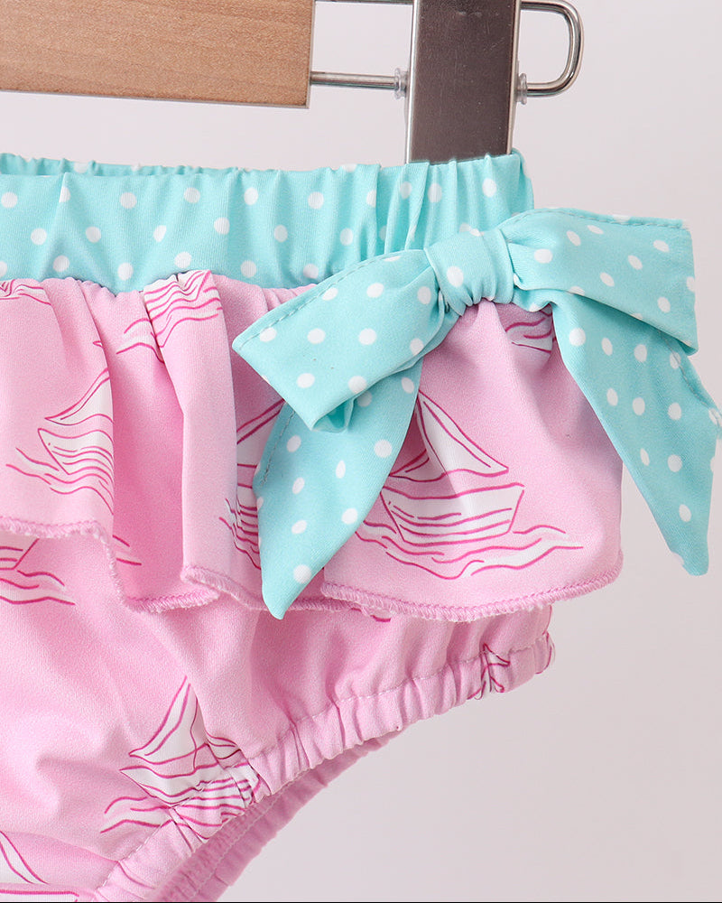 Pink swim bottoms with a blue polka dot bow on a white background