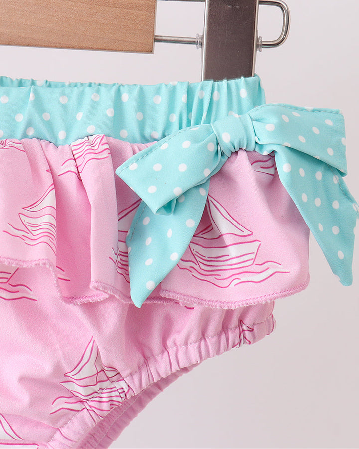 Pink swim bottoms with a blue polka dot bow on a white background