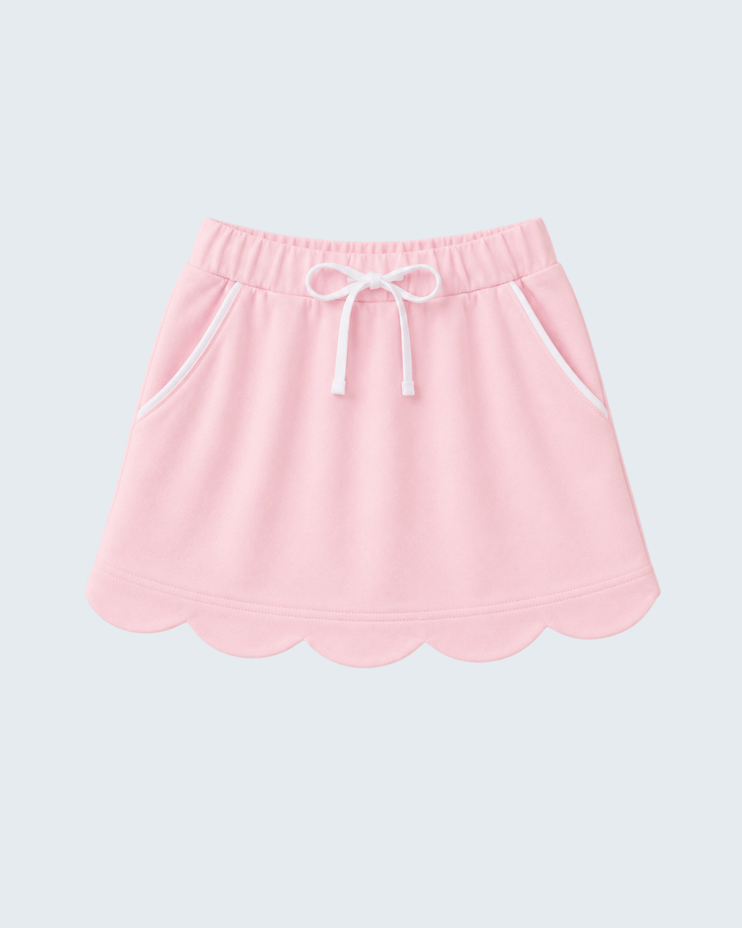 A light pink skort with a scalloped hem, white drawstring, and white piping details, shown against a light gray background.