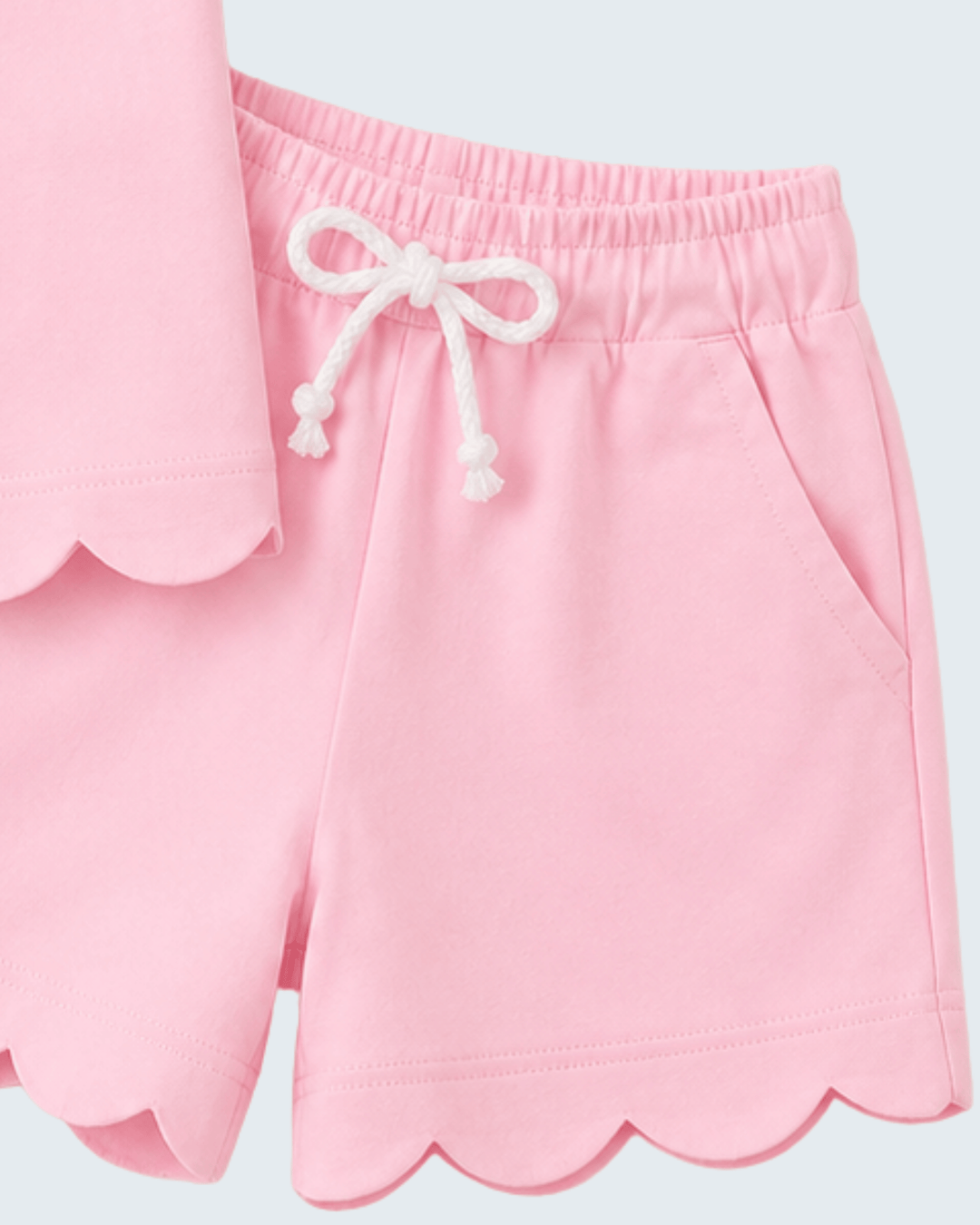 Pink shorts with scalloped hem and white drawstring on a light gray background