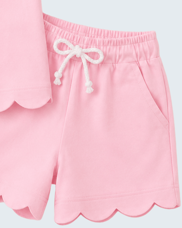 Pink shorts with scalloped hem and white drawstring on a light gray background