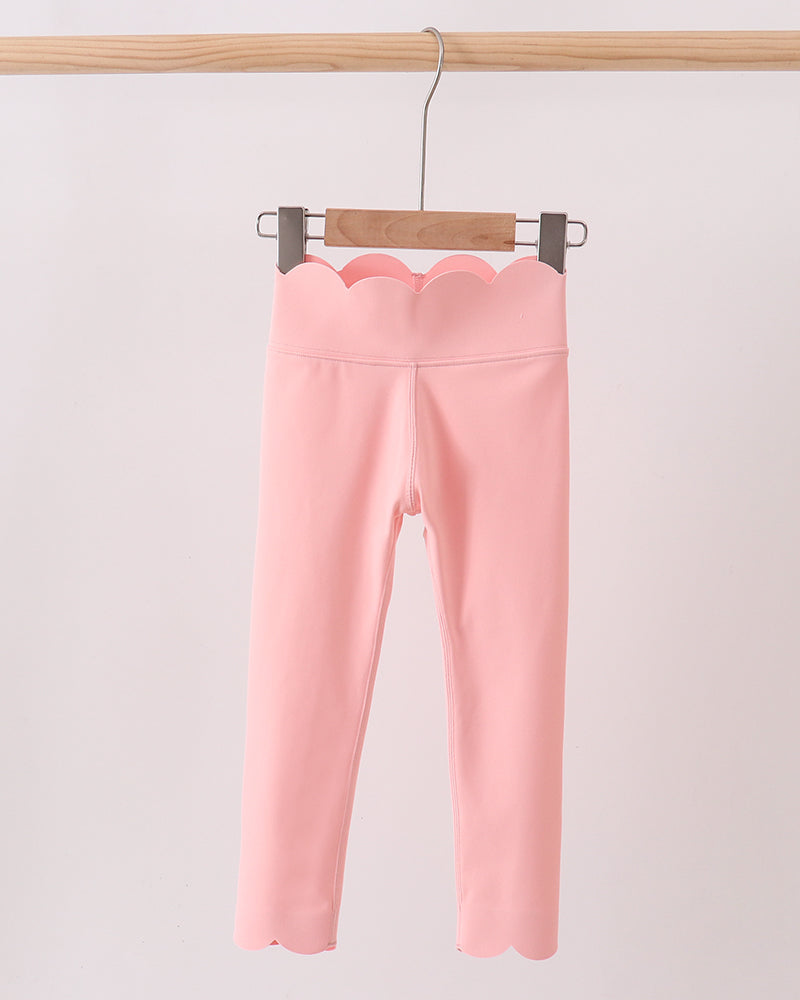 Pink leggings hanging on a wooden hanger against a light pink background