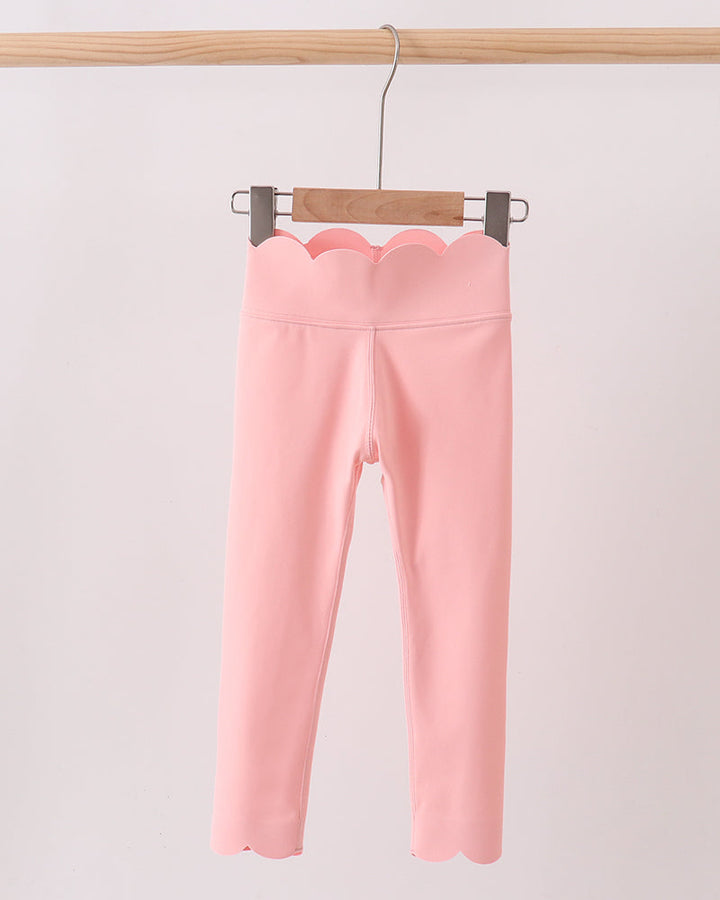Pink leggings hanging on a wooden hanger against a light pink background