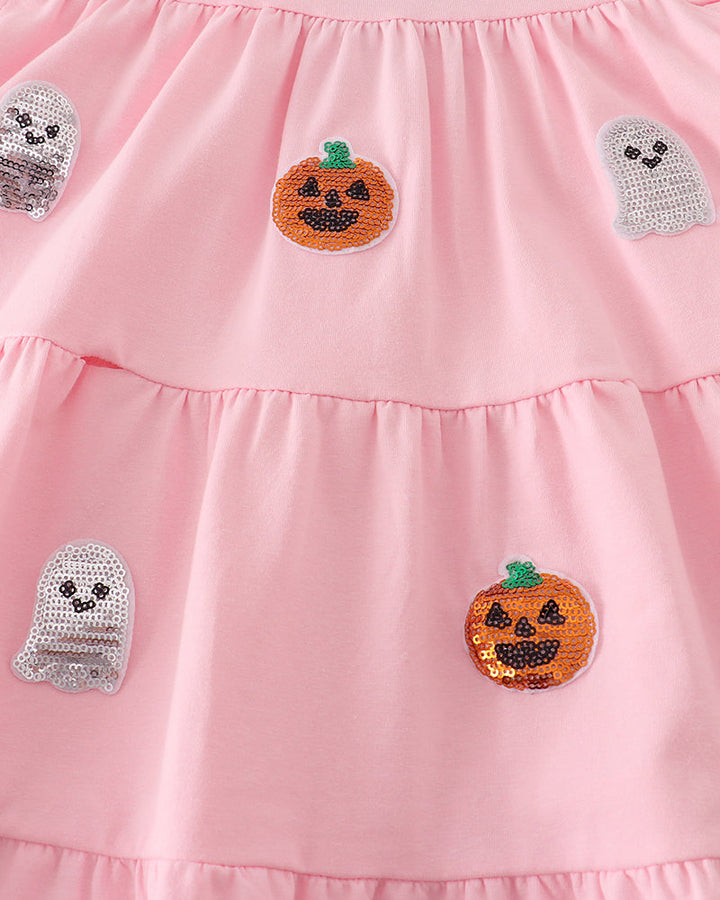 A close-up of a pink tiered dress featuring sequined pumpkin and ghost appliques.