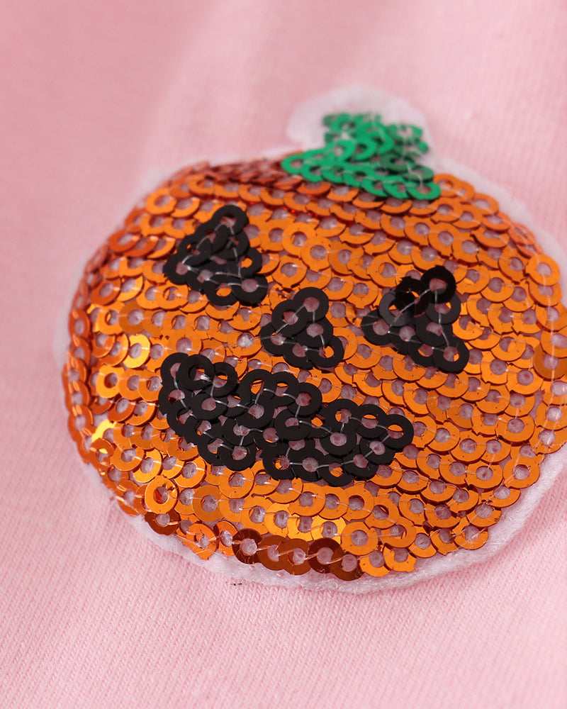 A close-up of a pumpkin-shaped sequin patch with a green stem and black sequin facial features on a pink fabric background.