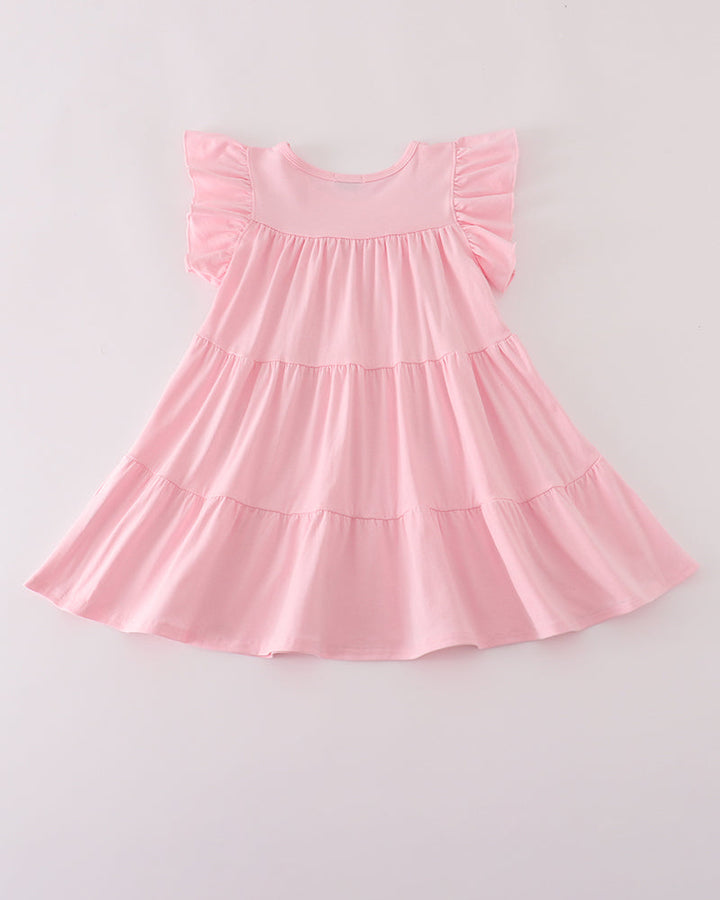 A light pink tiered baby dress with ruffled cap sleeves, laid flat against a light gray background.
