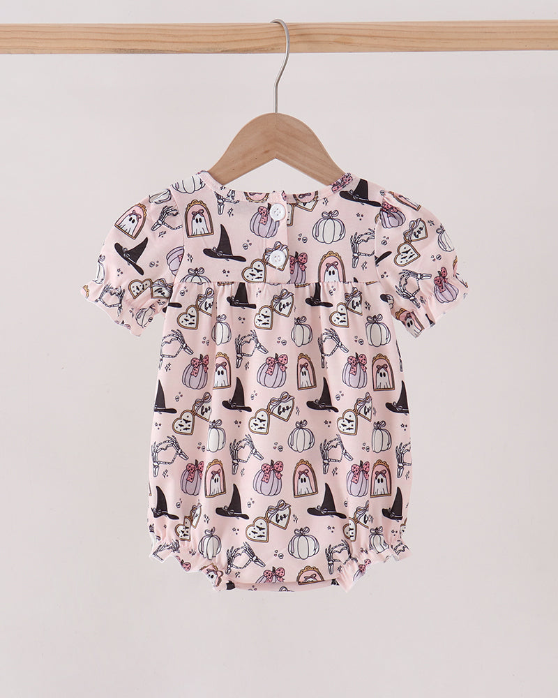 A baby short-sleeve romper in light pink with a black and white Halloween-themed print of pumpkins, ghosts, and witches, hanging on a wooden hanger.