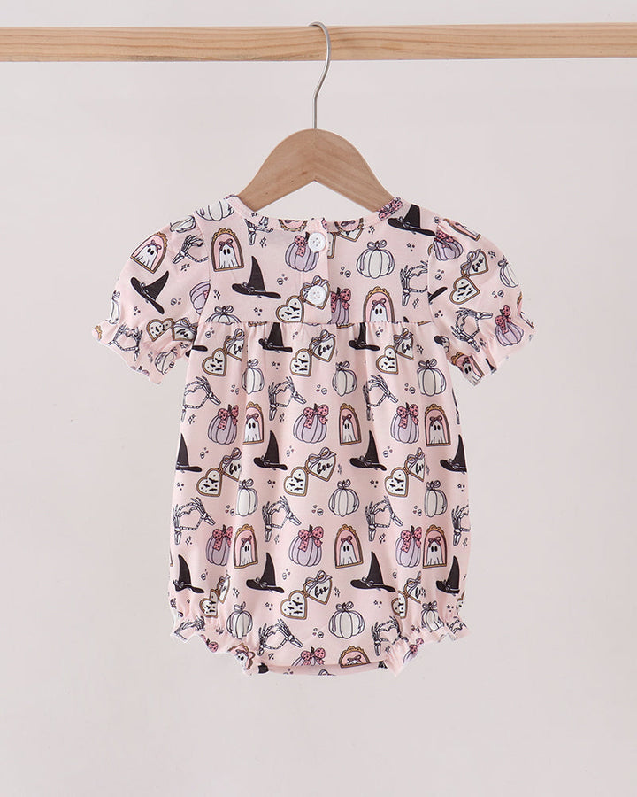 A baby short-sleeve romper in light pink with a black and white Halloween-themed print of pumpkins, ghosts, and witches, hanging on a wooden hanger.