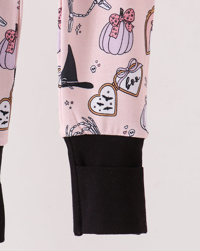 A close-up of a romper with a light pink Halloween-themed print featuring pumpkins, a witch hat, bats, and a skeleton hand, finished with a solid black ribbed cuff.