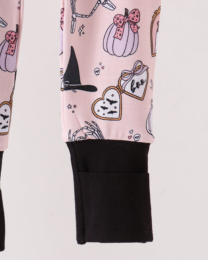 A close-up of a romper with a light pink Halloween-themed print featuring pumpkins, a witch hat, bats, and a skeleton hand, finished with a solid black ribbed cuff.