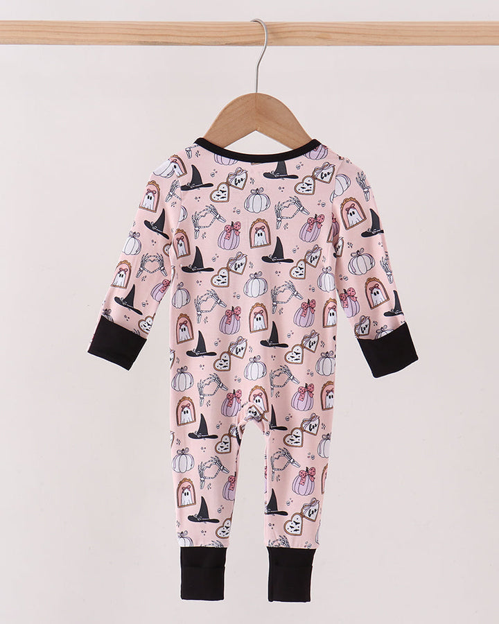 A baby long-sleeve footless pajama romper in light pink with a Halloween print of pumpkins, ghosts, and witch hats, hanging on a wooden hanger against a light beige wall.