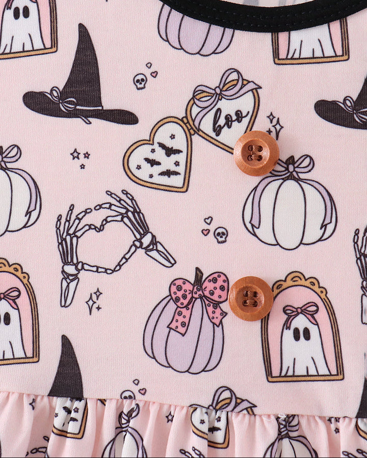 Close-up of a light pink Halloween-themed garment with a black trim and an all-over print of pumpkins, ghosts, witch hats, skeleton hands, and heart-shaped pockets with two brown buttons.