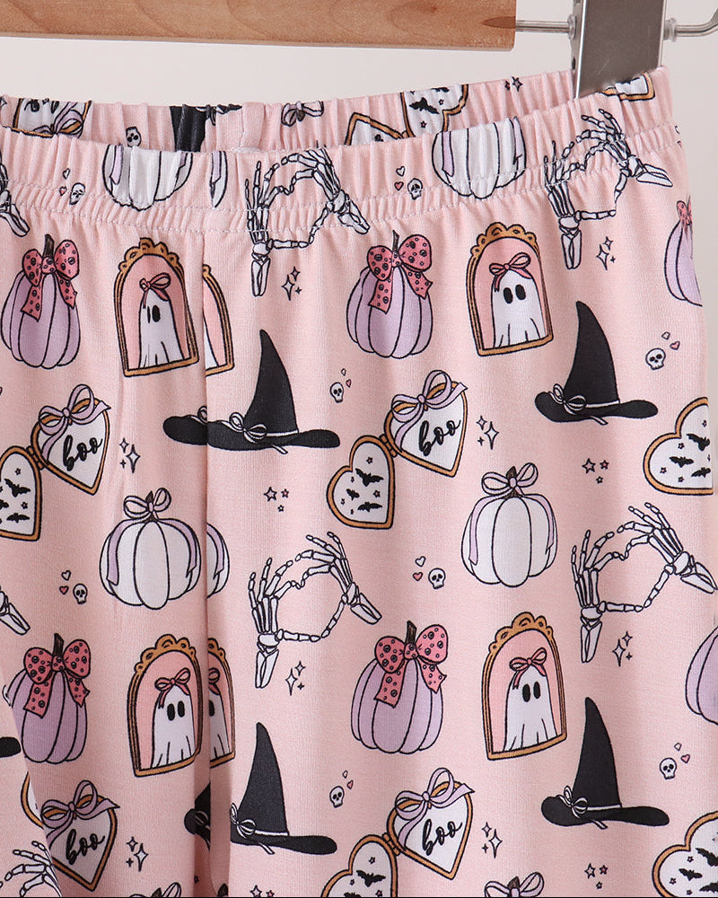 Pink Halloween-themed lounge pants with an all-over print of pumpkins, ghosts, witch hats, skeleton hands, and candy corn, hanging from a wooden hanger.