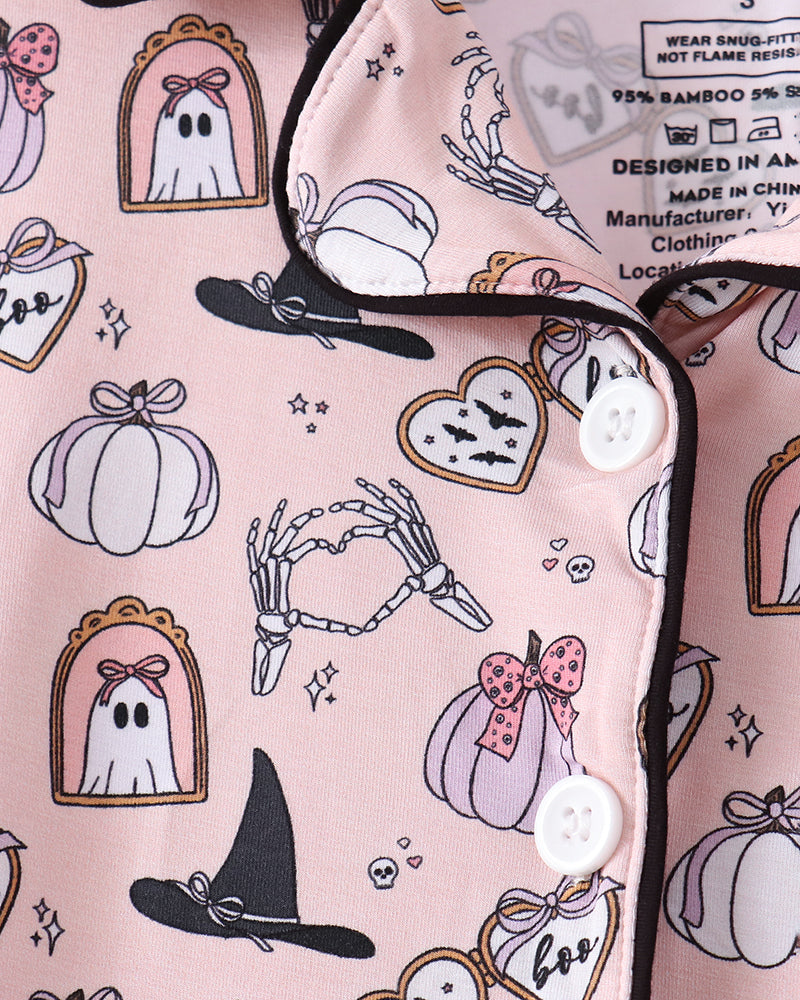 Pink pajama top with a Halloween print featuring ghosts, pumpkins, witch hats, skeleton hands, bats, and hearts, shown in a close-up of the fabric and buttoned collar.